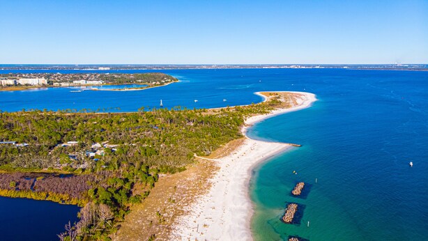 Luftaufnahme einer Küstenlandschaft mit Strand, klarem blauen Wasser und einem bewaldeten Gebiet.