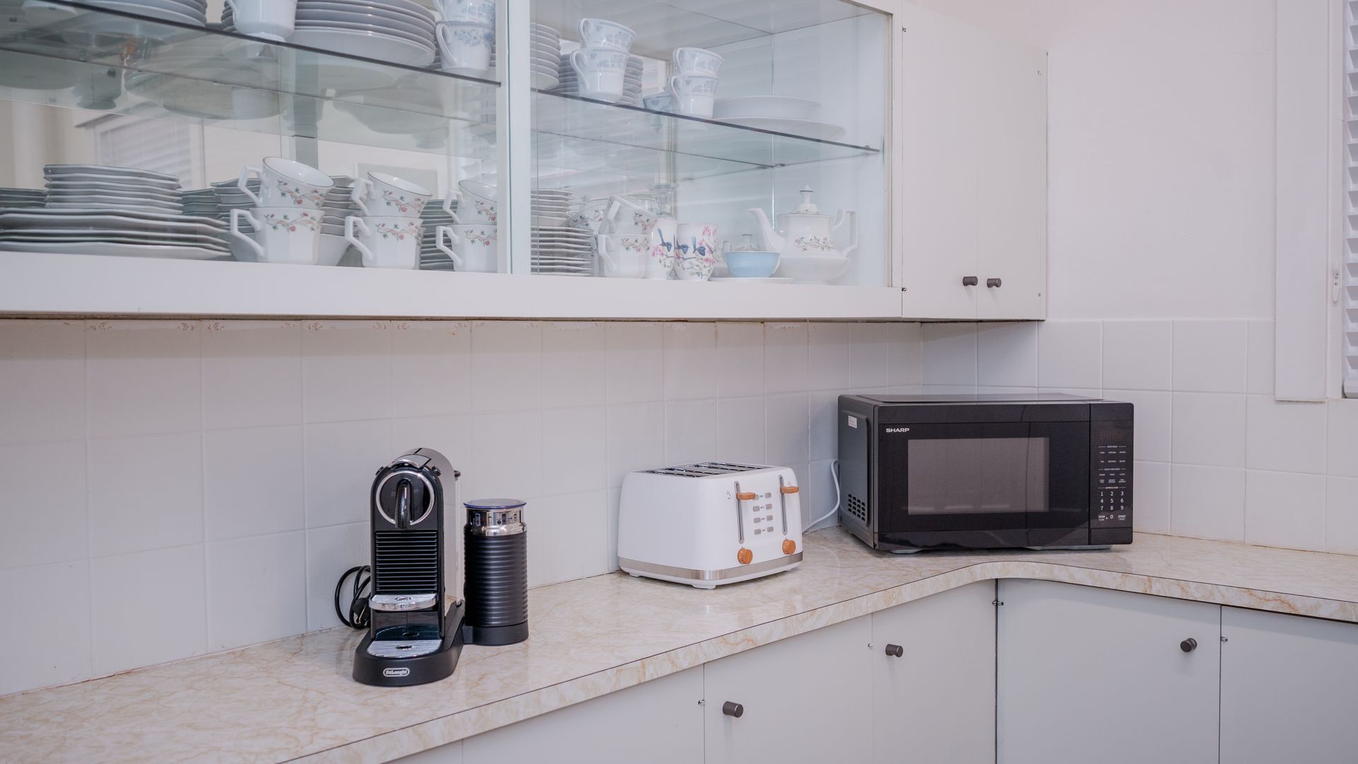A kitchen with a microwave, toaster, and coffee maker on the counter, and a glass cabinet above with dishes.