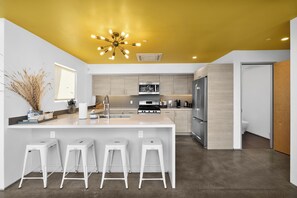 Een moderne keuken met een centraal eiland, barstoelen en een geel plafond.