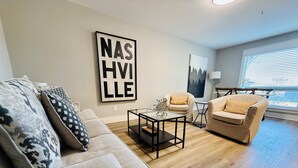 A modern living room with a sofa, armchairs, a coffee table, and a large wall art piece. - Downtown Nashville Condo • 1 Mile to Broadway • Pool & Parking (Nashville)