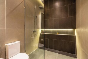 A modern bathroom with a glass-enclosed shower, a toilet, and a shelf with toiletries. - Tropical Villa Raya (Ungasan)