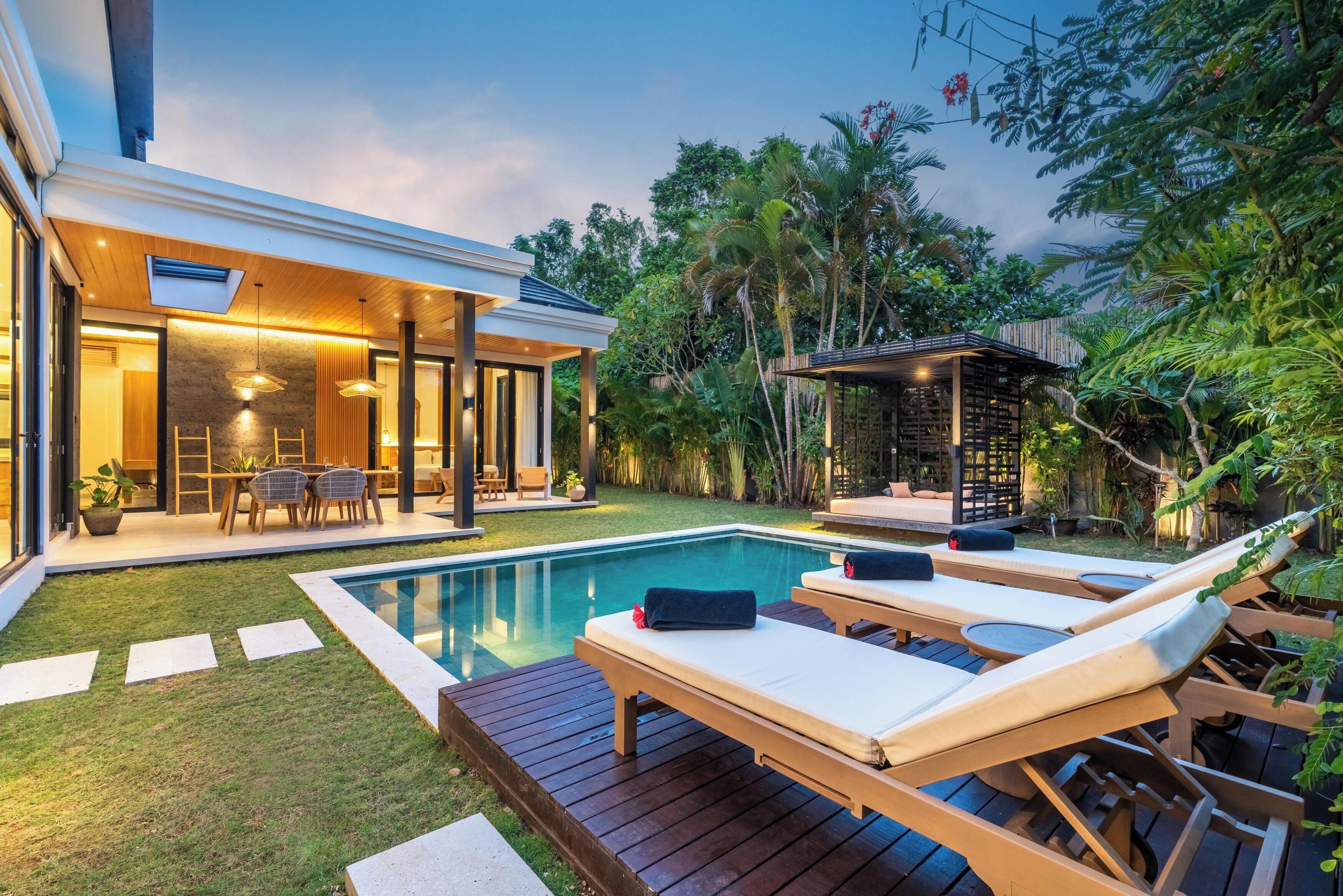 Un espace piscine extérieur moderne, doté de chaises longues, d’une terrasse en bois et d’un patio fermé par des baies vitrées.