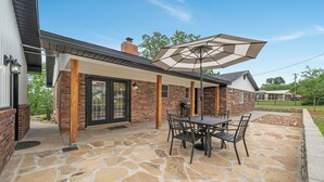 Une terrasse avec un sol en pierre, une table et des chaises, et un grand parasol.