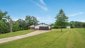 Une maison de plain-pied avec un garage, entourée d’une pelouse bien entretenue et d’arbres.
