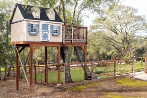 A wooden treehouse with a balcony, situated in a wooded area.