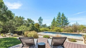 A wooden deck with two lounge chairs facing a swimming pool, surrounded by lush greenery and trees. - Glen Ellen Wine Country Retreat w/pool, hot tub, Bocce, tree-house & more (Glen Ellen)