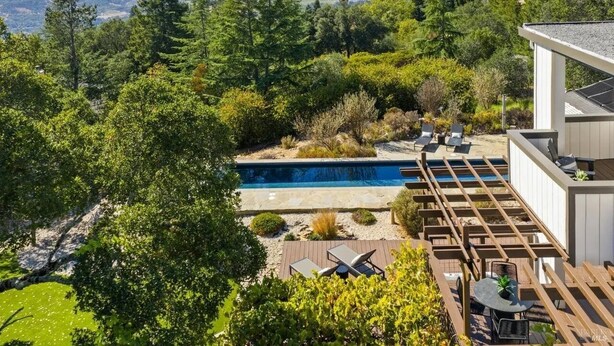 A pool with a wooden deck and lounge chairs, surrounded by lush greenery and a mountainous backdrop. - Glen Ellen Wine Country Retreat w/pool, hot tub, Bocce, tree-house & more (Glen Ellen)