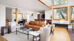 A spacious living area with a large window, a sofa, a coffee table, and a fireplace. - Glen Ellen Wine Country Retreat w/pool, hot tub, Bocce, tree-house & more (Glen Ellen)