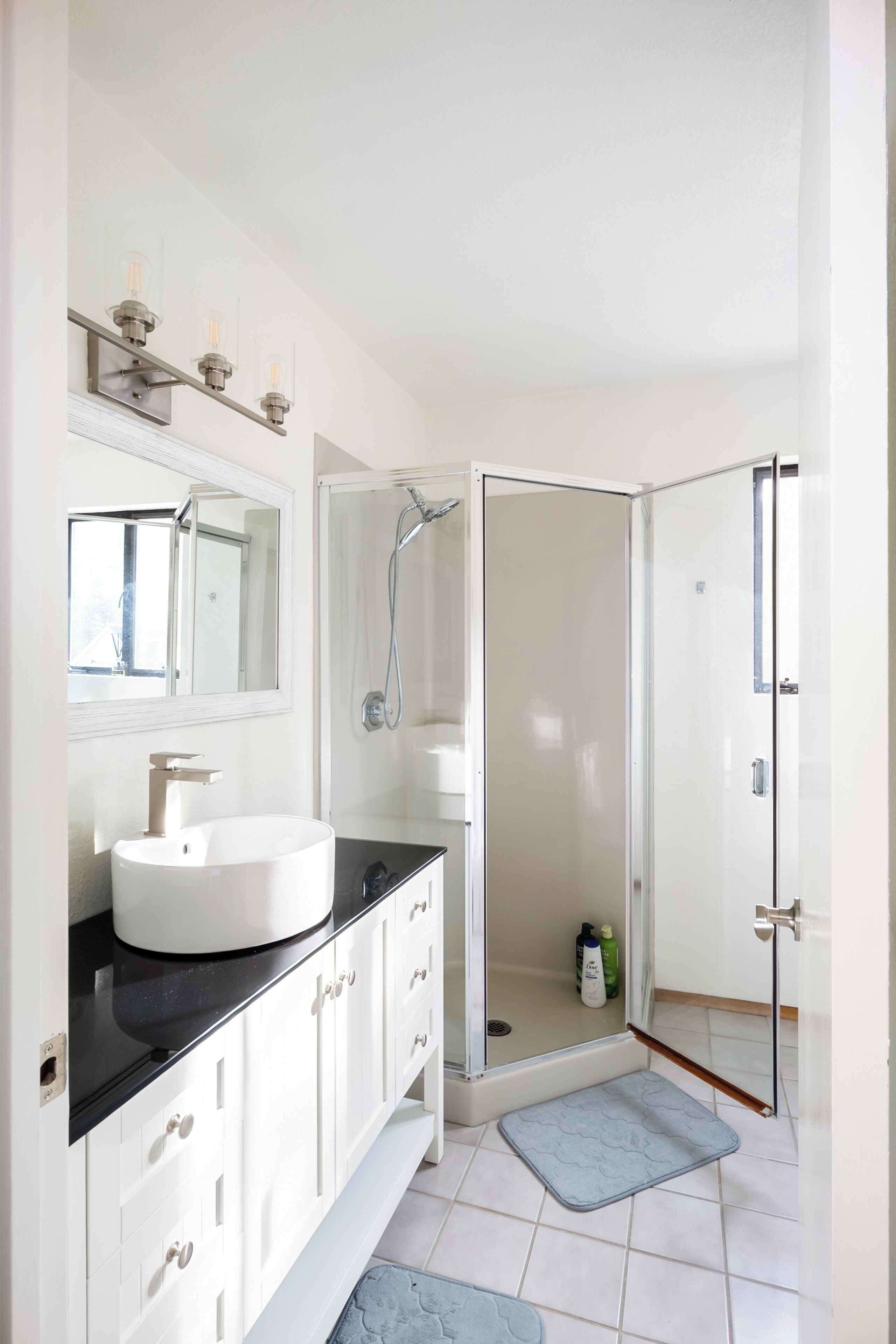 Un baño moderno con lavamanos, espejo y ducha blancos.
