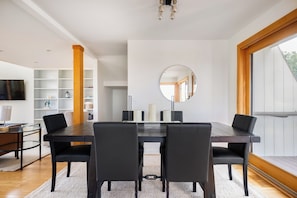 Une salle à manger moderne avec une table en bois foncé, des chaises noires, un grand miroir rond et une grande fenêtre.