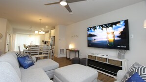 Een moderne woonkamer met een flatscreen televisie, een plafondventilator en een eethoek op de achtergrond.