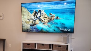 Een flatscreen televisie aan een wand bevestigd, een aquarium eronder en een witte entertainmentkast met manden.