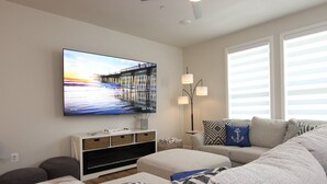 Een woonkamer met een flatscreen televisie, een bank, een voetenbankje en een bijzettafeltje met lampen.