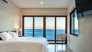Camera da letto con un letto grande, una sedia e vista sul mare tramite una porta scorrevole.