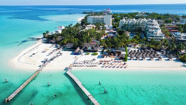 Vista aerea di una località balneare con un molo, spiaggia e bungalow sull'acqua.