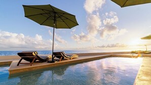 Una piscina a sfioro con lettini e ombrelloni, con vista sull'oceano.