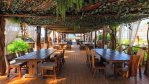 Area pranzo all'aperto con tavoli e sedie in legno, coperta da una pergola in legno con piante pendenti.