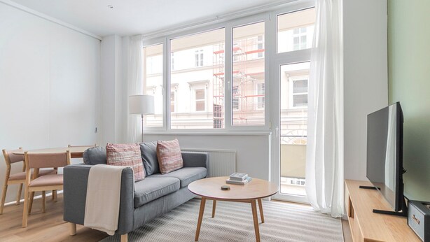 Ein modernes Wohnzimmer mit einem grauen Sofa, Holzstühlen, einem runden Couchtisch und einem Fernseher auf einem Holzboden.