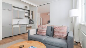 Eine moderne Wohnung mit grauem Sofa, einem Holztisch, einer Küche mit grauen Schränken und einem großen Fenster.