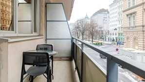 Ein Balkon mit Tisch und Stühlen, mit Blick auf eine Straße mit Gebäuden und einer Straßenbahn.