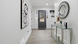 A hallway with a glass console table, a decorative mirror, and framed artwork on the walls. - Elegant 4BR Home in Grayson-Cozy, Modern & Relaxing Stay. (Grayson)