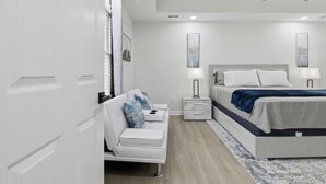 A modern bedroom with a white bed, bedside tables, a white sofa, and a ceiling fan. - Elegant 4BR Home in Grayson-Cozy, Modern & Relaxing Stay. (Grayson)