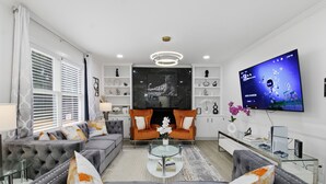 A modern living room with a grey sofa set, a glass coffee table, and a flat-screen TV mounted on the wall. - Elegant 4BR Home in Grayson-Cozy, Modern & Relaxing Stay. (Grayson)
