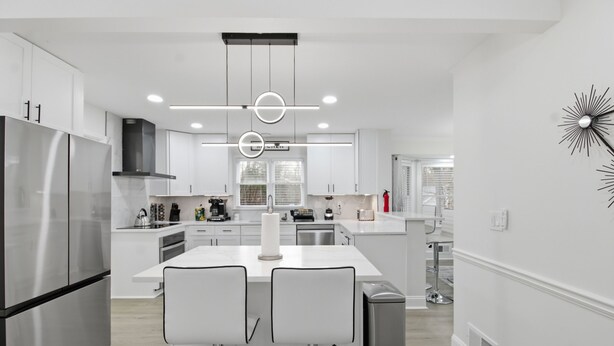 A modern kitchen with white cabinetry, stainless steel appliances, and a central island with bar stools. - Elegant 4BR Home in Grayson-Cozy, Modern & Relaxing Stay. (Grayson)