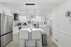A modern kitchen with white cabinetry, stainless steel appliances, and a central island with bar stools. - Elegant 4BR Home in Grayson-Cozy, Modern & Relaxing Stay. (Grayson)