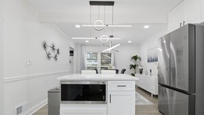 A modern kitchen with white cabinetry, a stainless steel refrigerator, and pendant lighting. - Elegant 4BR Home in Grayson-Cozy, Modern & Relaxing Stay. (Grayson)