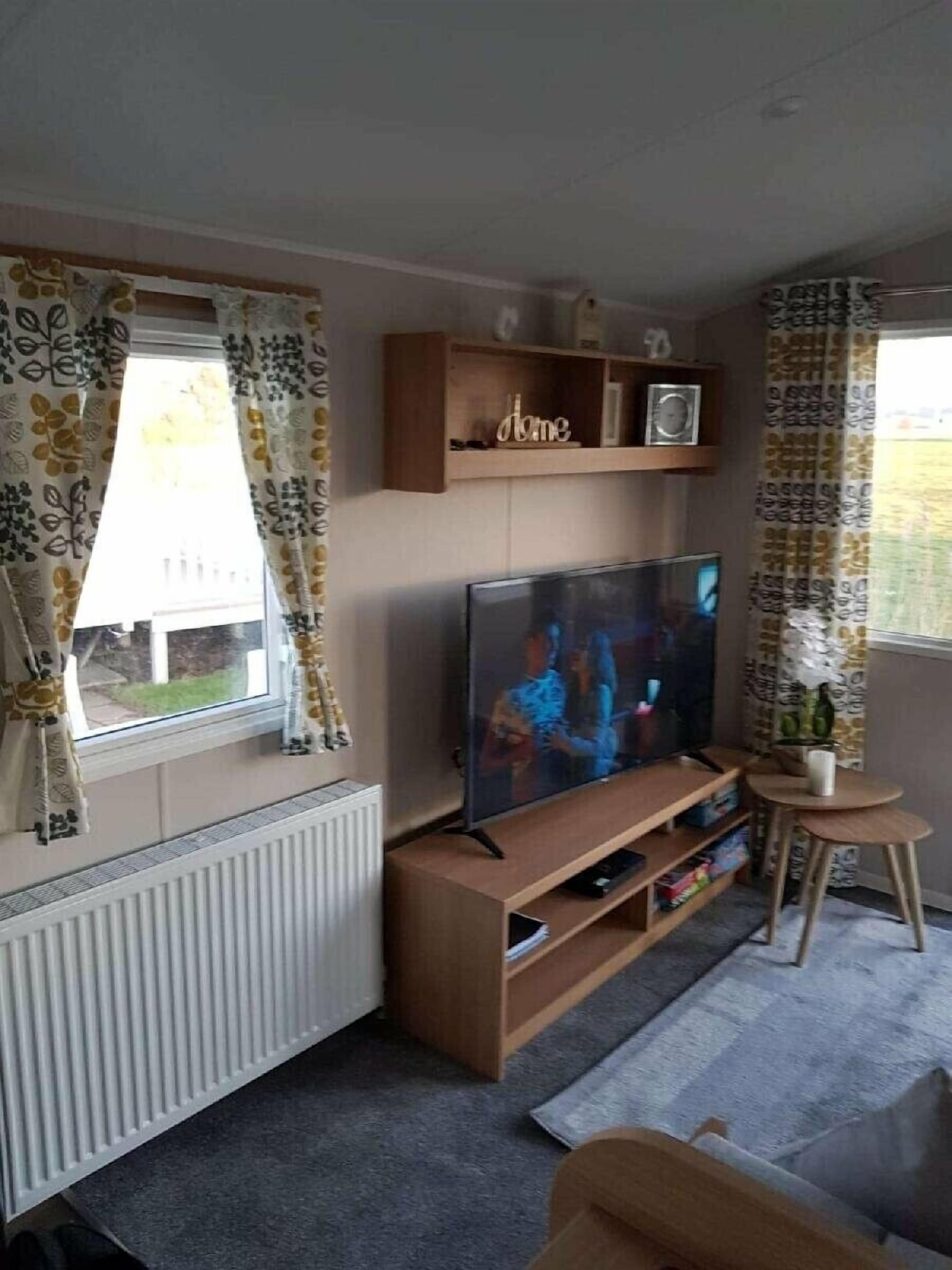 A living room with a TV, wooden shelves, a small table, and a radiator.