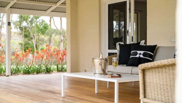 Un espace extérieur aménagé avec une zone salon couverte, dotée d’un plancher en bois, d’une table blanche et d’un canapé agrémenté de coussins noirs et blancs.