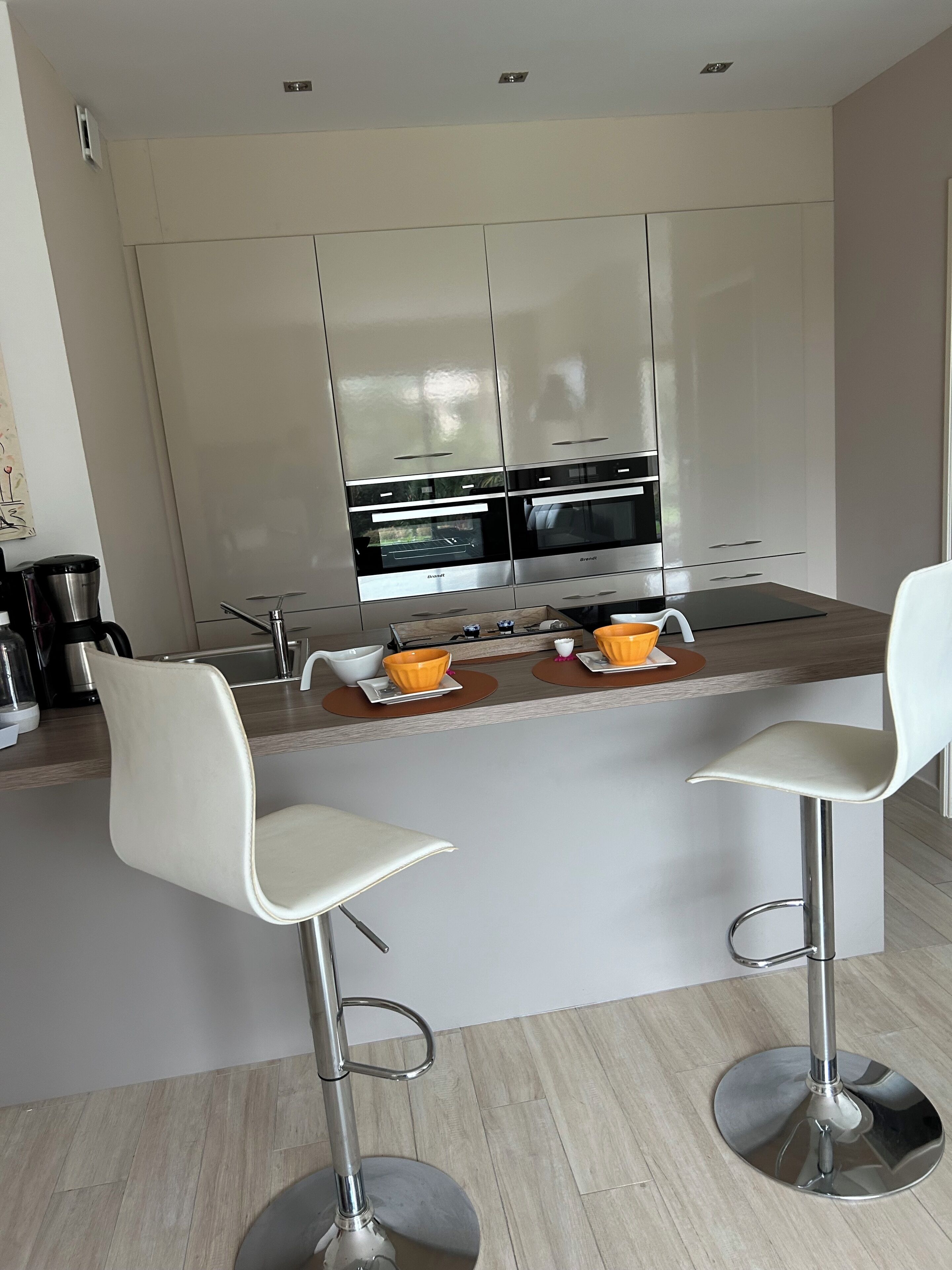 A modern kitchen with two bar stools, a built-in oven, and a coffee machine.