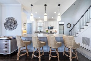 A modern kitchen with a central island, bar stools, and pendant lighting.
