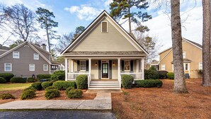 A two-story house with a front porch, a chimney, and a small front yard with trimmed bushes and a tree.