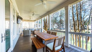 A covered outdoor deck with a wooden table and chairs, a ceiling fan, and a view of the surrounding area.