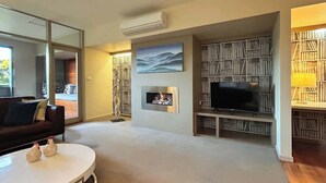A modern living room with a flat-screen TV, a fireplace, a bookshelf, and a large mirror. - Villa 7 Hepburn Springs (Hepburn Springs)