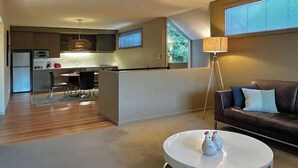 A modern living room with a sofa, a coffee table, and a dining area with a kitchen in the background. - Villa 7 Hepburn Springs (Hepburn Springs)
