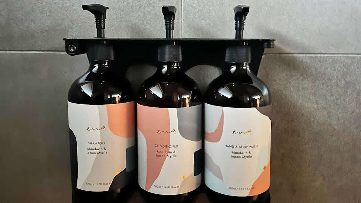 Three bottles of shampoo, conditioner, and hand & body wash with pump dispensers, labeled 'ena' and containing Mandarin & Lemon Myrtle.