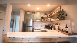 Una cocina moderna con un refrigerador de acero inoxidable, una estufa y un microondas. Hay repisas de madera sobre la encimera con varios utensilios de cocina y plantas.
