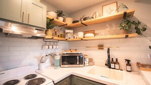 Una cocina moderna con gabinetes blancos, estufa, microondas y repisas de madera sobre el mostrador.