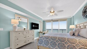 Ein Schlafzimmer mit Bett, Kommode, Fernseher, Deckenventilator und einem Balkon mit Aussicht.