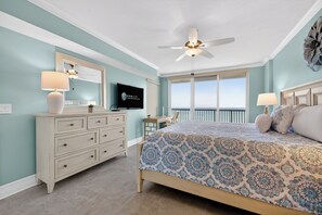 Ein Schlafzimmer mit Bett, Kommode, Fernseher, Deckenventilator und einem Balkon mit Aussicht.
