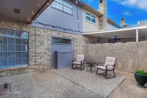 A covered patio area with two rocking chairs and a small table, a gray door, and a stone wall.