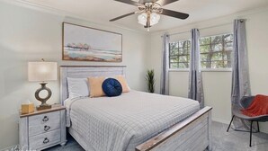 A bedroom with a bed, a nightstand, a lamp, a ceiling fan, a window with curtains, and a chair. - Serene & Spacious Townhouse with Private Patio (Shreveport)