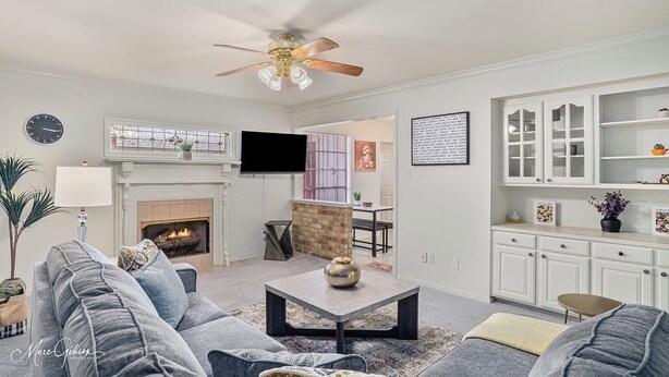 A living room with a fireplace, a ceiling fan, and a television. - Serene & Spacious Townhouse with Private Patio (Shreveport)