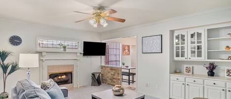A living room with a fireplace, a ceiling fan, and a television.