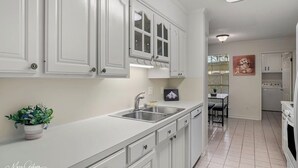 A modern kitchen with white cabinetry, a double sink, and a dining area with a table and chairs. - Serene & Spacious Townhouse with Private Patio (Shreveport)