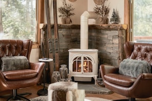 A cozy room with a stone fireplace, a white wood-burning stove, leather armchairs, and a rustic decor. - Tahoe Park Cabin: Hot Tub, Fireplace + Private Beach (Tahoe City)