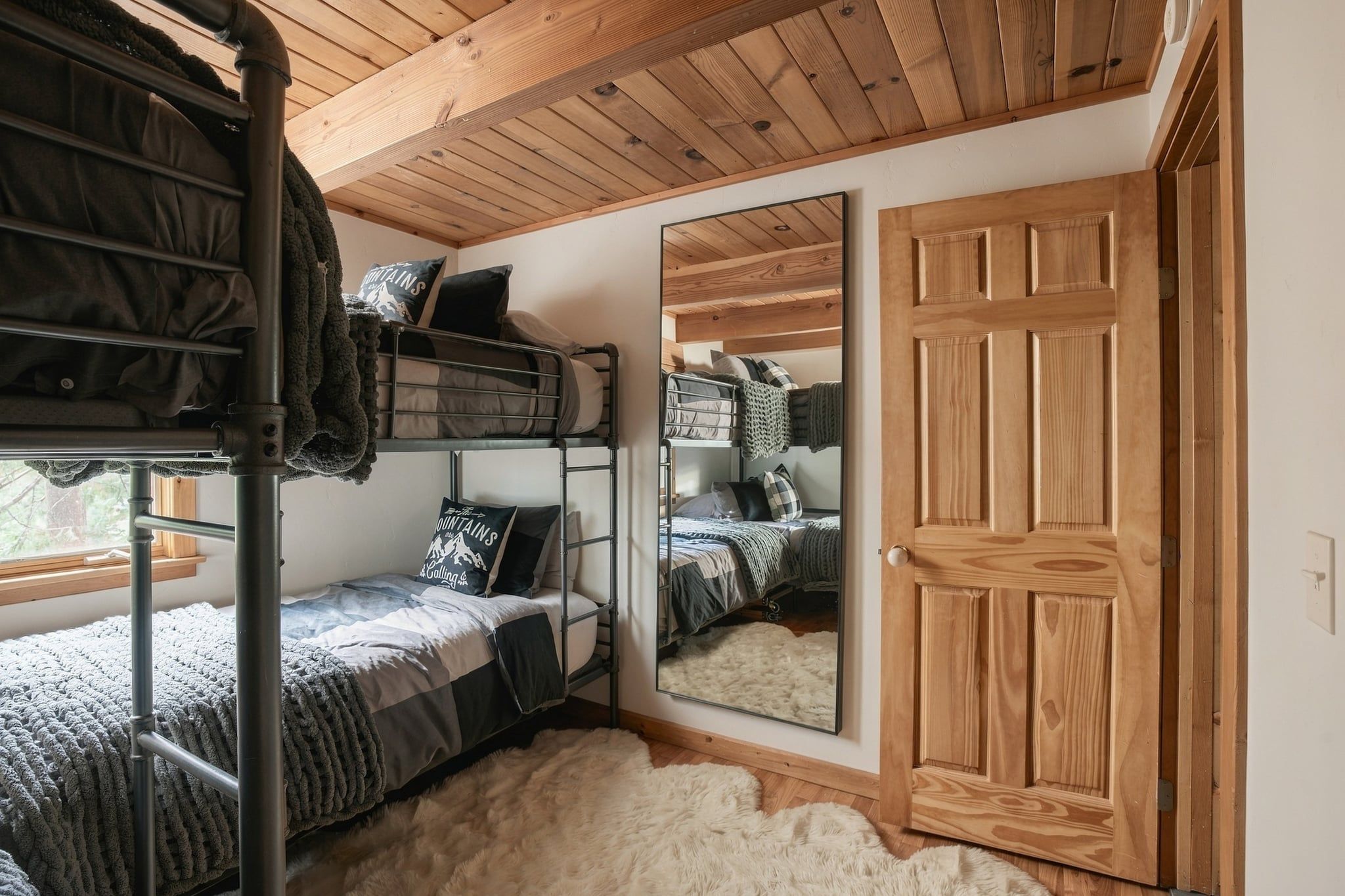 A bunk bed room with a wooden ceiling, a large mirror, and a wooden door.